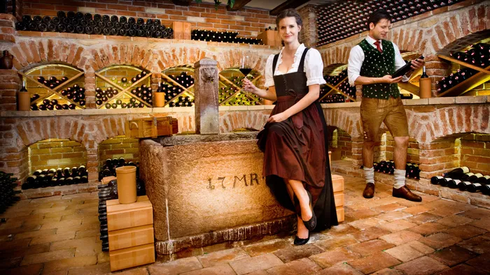 Paar in traditioneller bayerischer Kleidung in rustikalem Weinkeller mit Weinflaschenregalen